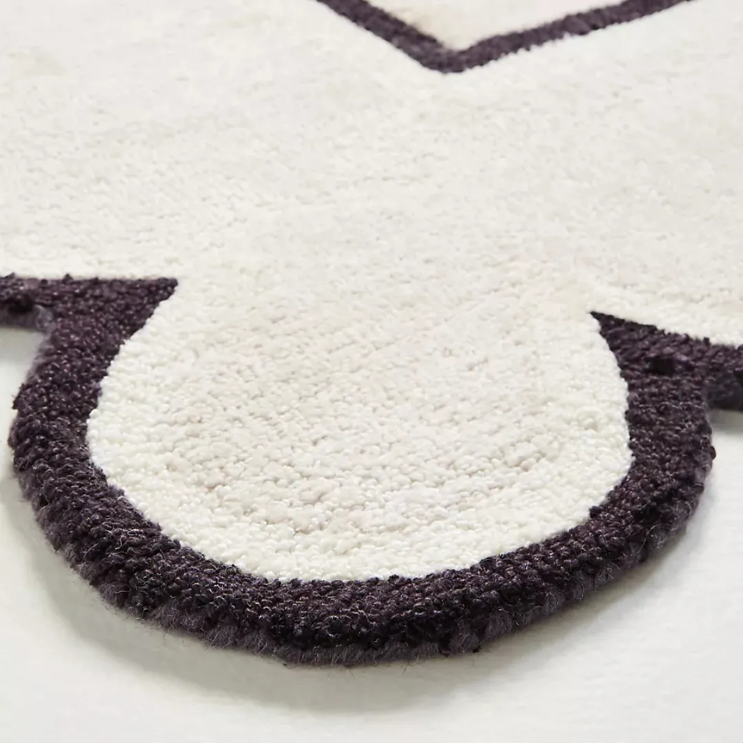 Side angle of hand tufted white rug showing raised texture and scalloped shape