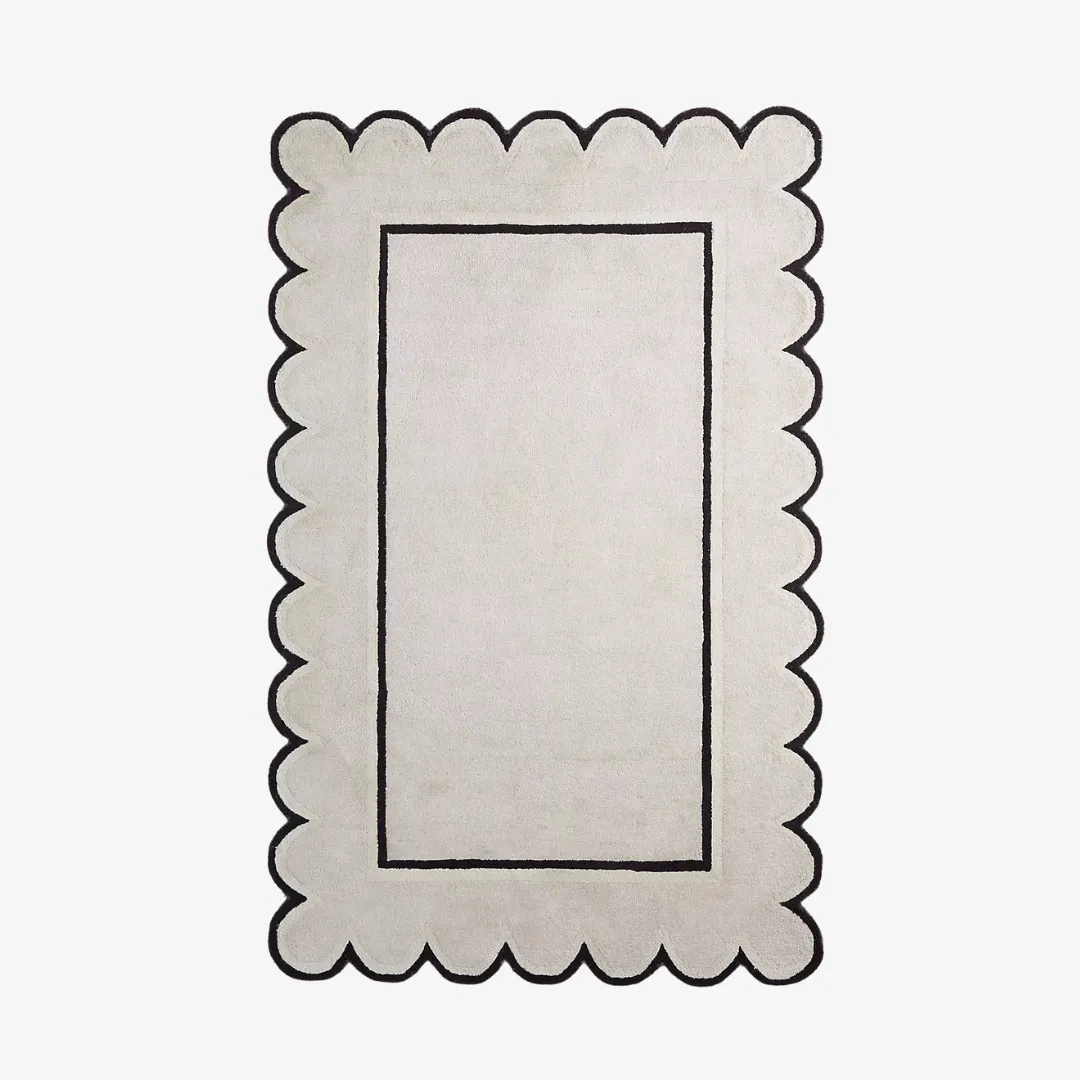 White scallop edge hand tufted rug with black border on ivory background, shown flat on white floor