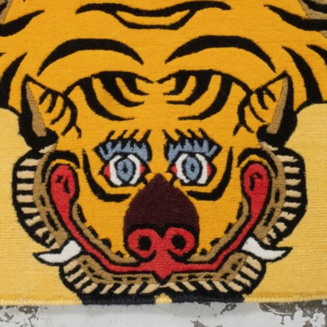 Yellow Tibetan tiger rug with bold black stripes, blue eyes, and red facial details, displayed on a concrete surface.