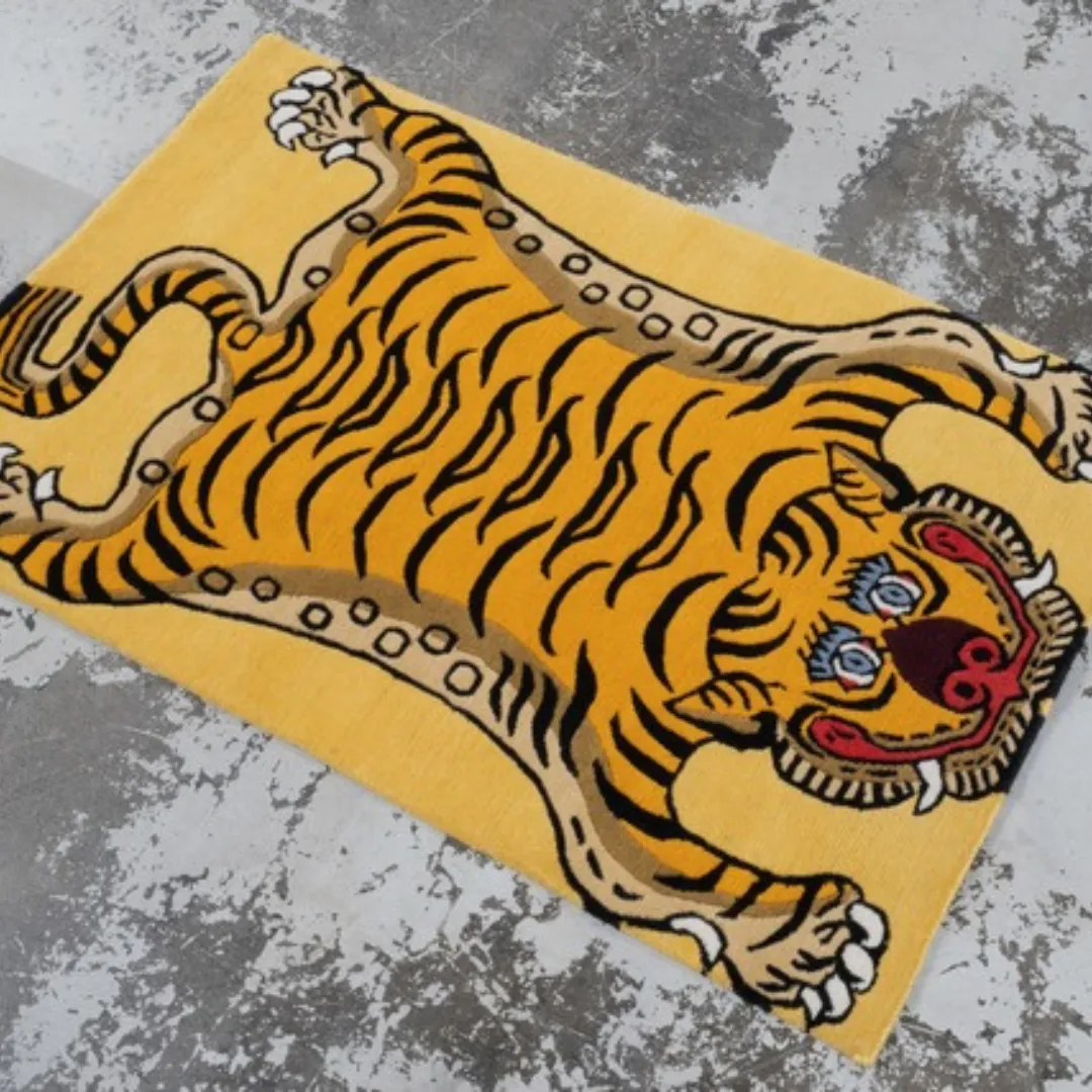 Yellow Tibetan tiger rug with bold black stripes, blue eyes, and red facial details, displayed on a wooden surface.