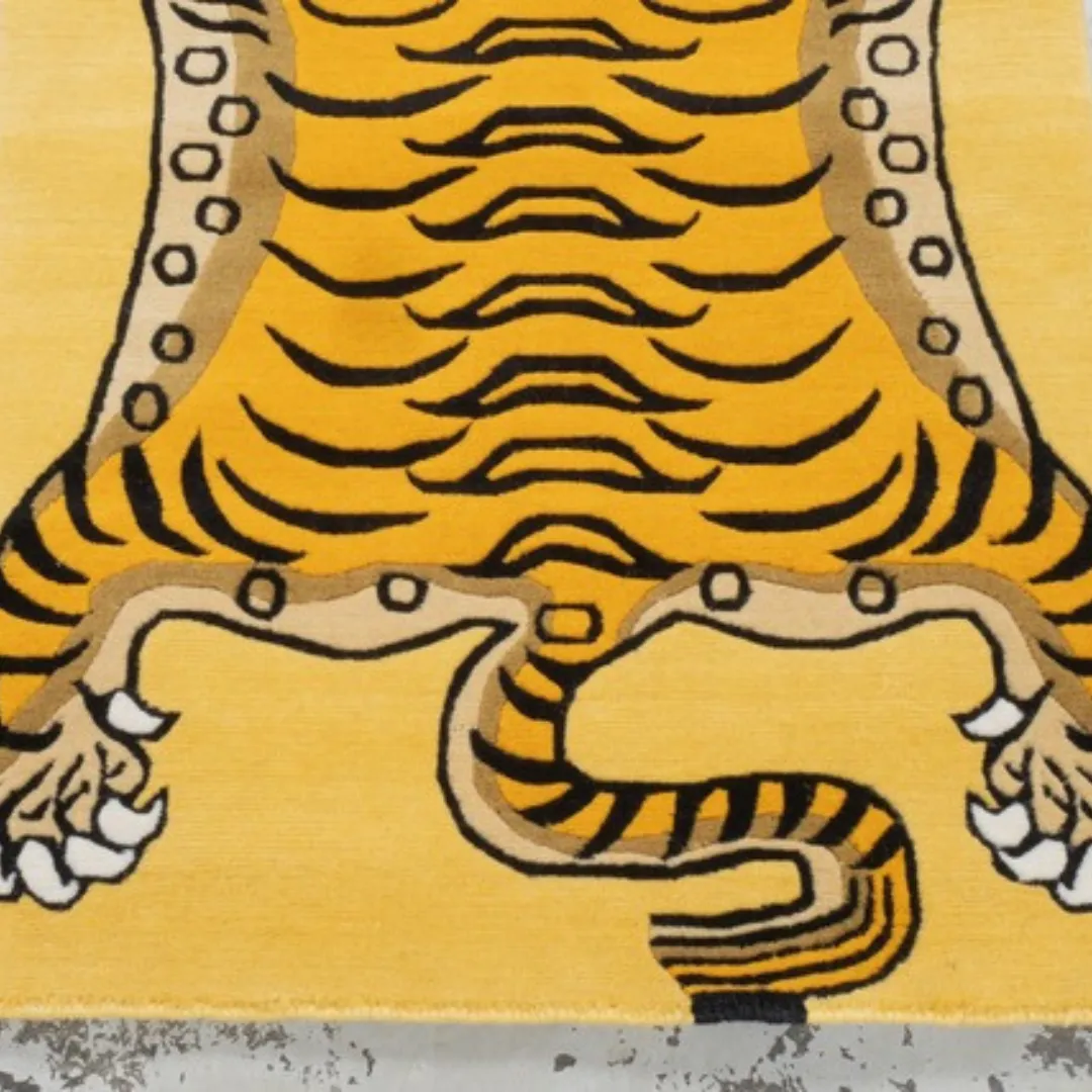 Hand tufted yellow Tibetan tiger rug with bold black stripes, blue eyes, and red facial details, displayed on a concrete surface.