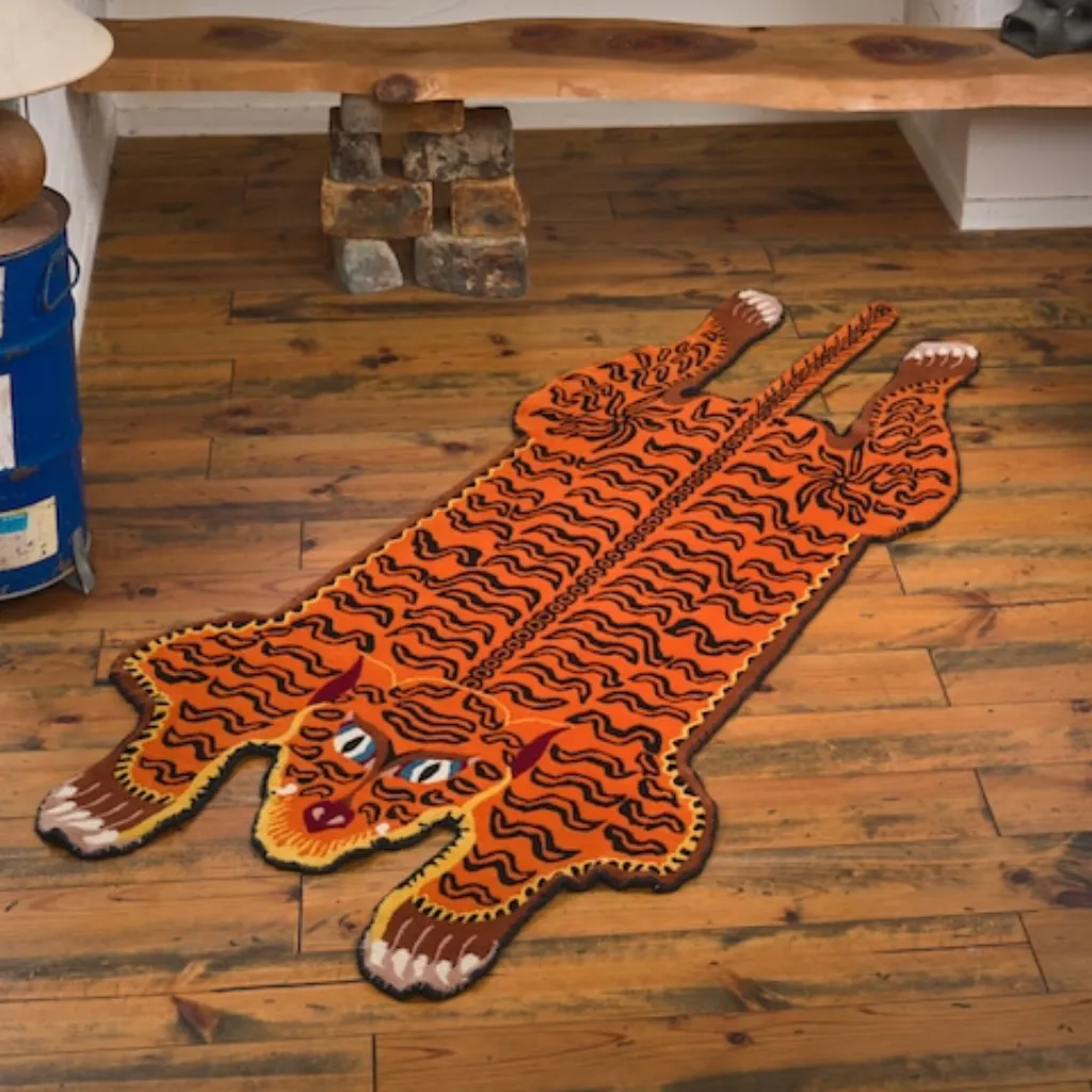 amber raja orange tiger skin shaped rug wood floor High angle view of the full Amber Raja rug placed on a rustic wooden floor, showcasing the traditional Tibetan tiger skin shape with "paws" and a tail.