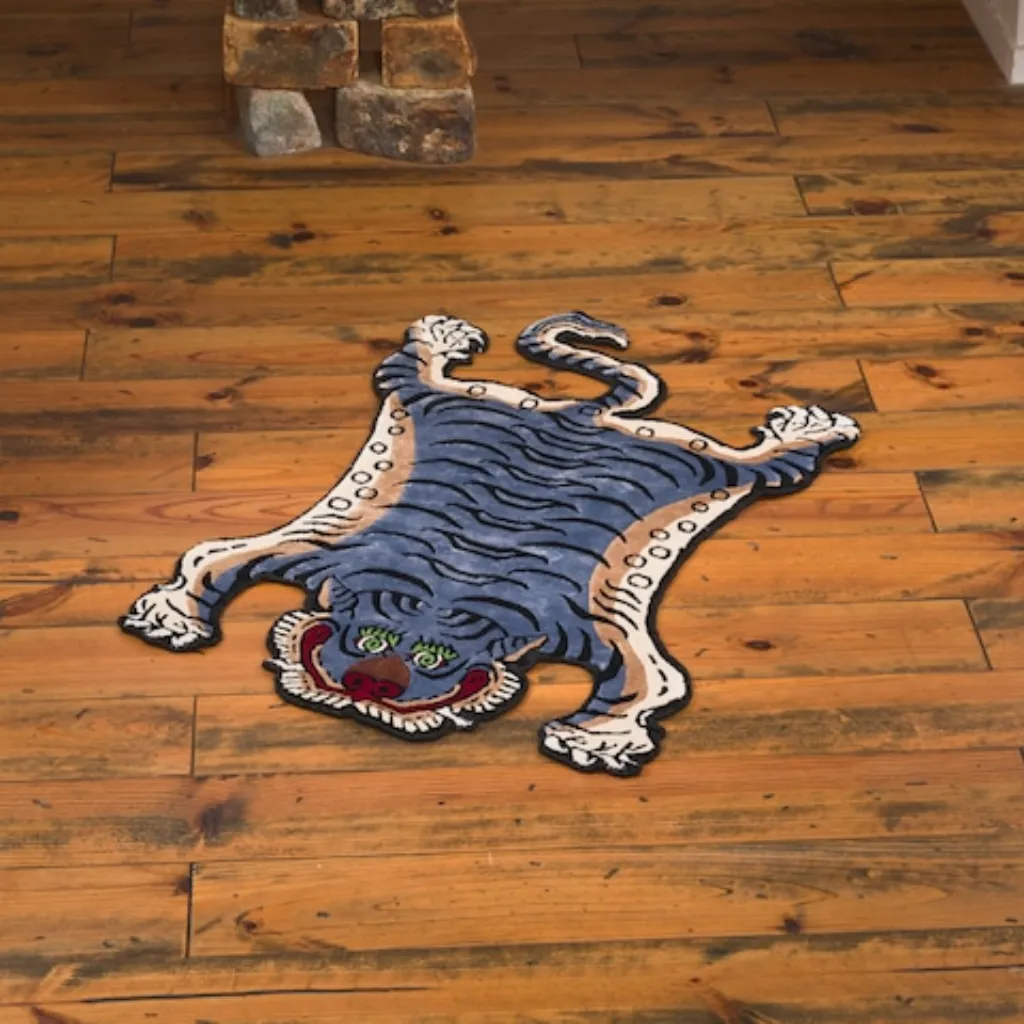 ashen claw tibetan tiger skin shaped rug wood floor High angle view of the full Ashen Claw rug placed on a rustic wooden floor, showcasing the traditional Tibetan tiger skin shape in a muted blue-grey and tan color palette.