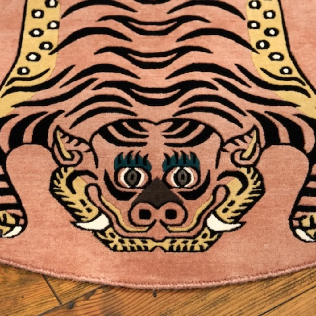 petal prawl pink tibetan tiger rug face detail Close-up top down view of the Petal Prawl Tibetan Rug, focusing on the stylized tiger face with teal eyes, sharp teeth, and black stripes on a soft pink wool background.