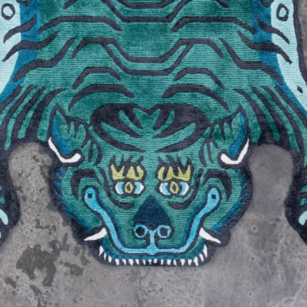 tidal prowl teal tibetan tiger rug head detail Close-up top down view of the Tidal Prowl Tibetan Rug, focusing on the stylized tiger face with bright eyes and black wavy stripes set against a refreshing teal blue background.