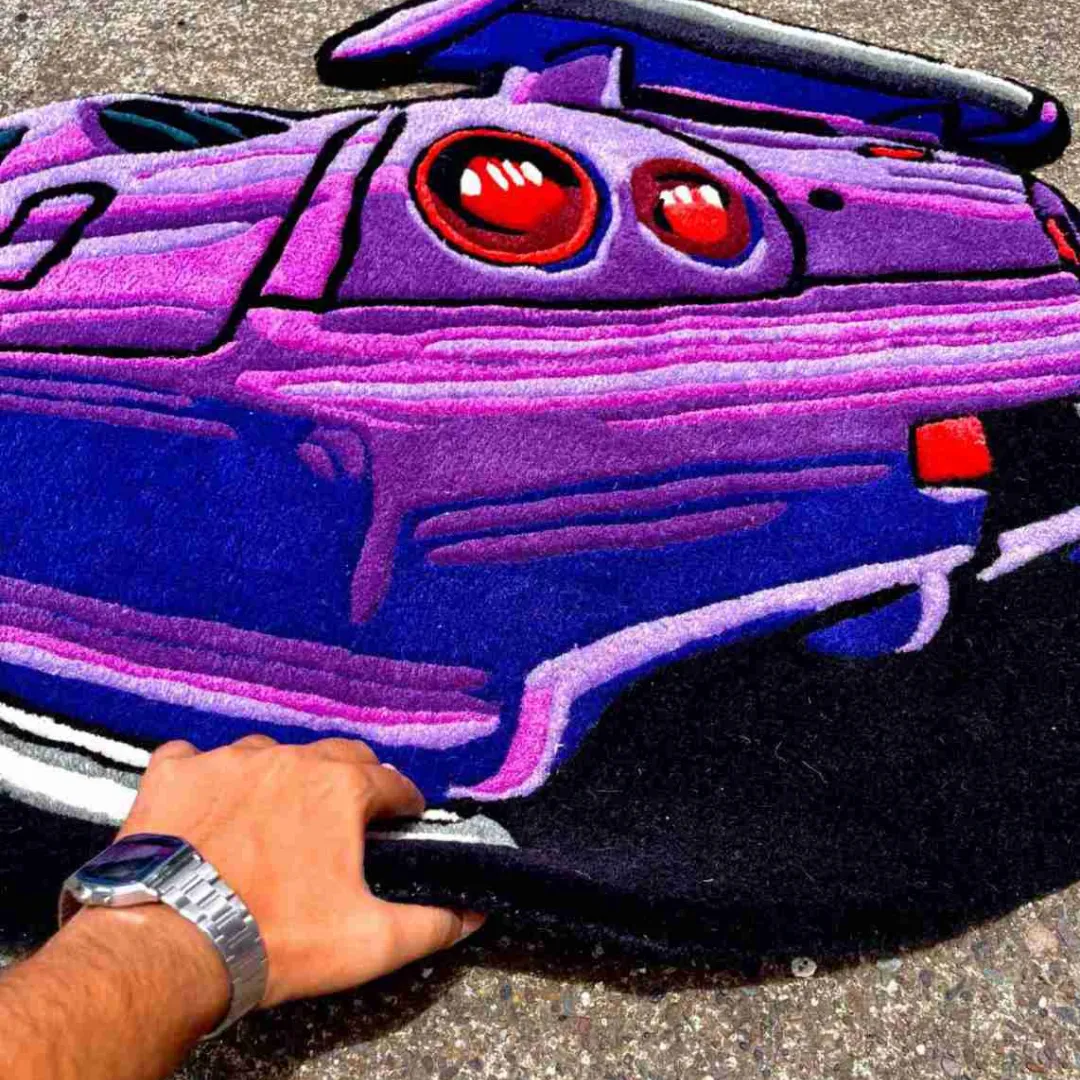 arrow crest rug tufted wool quality Perspective view of the Arrow Crest rug with a hand lifting the edge, showcasing the thick hand-tufted wool pile and the vibrant shading of the purple bumper.