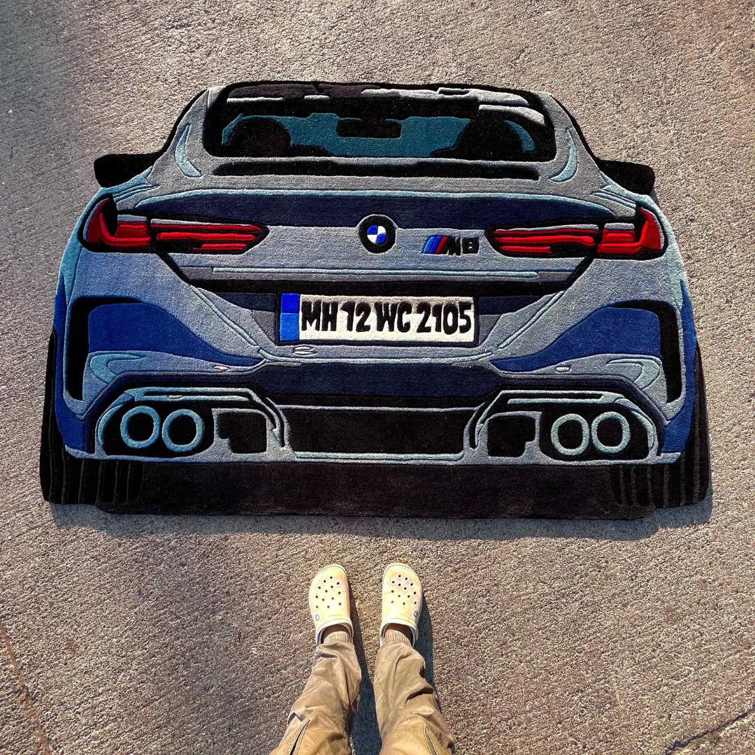 iron nomad grey sports car rug Top down view of the Iron Nomad rug featuring a custom die-cut design of a grey BMW M8 rear bumper with detailed taillights, exhaust, and badging.