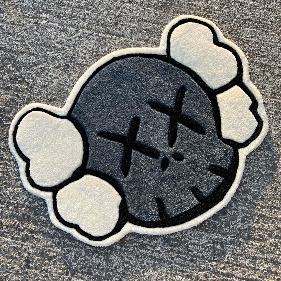 Angled close-up view of the Gravine Emblem rug on a textured road, highlighting the dense, plush hand-tufted grey and white wool texture and the sharply carved black details of the face.