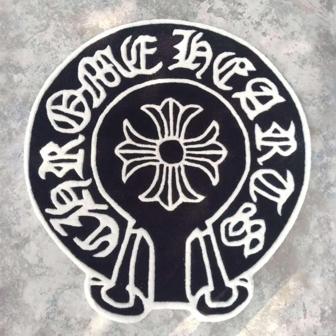 Top-down view of the Midnight Noir Crest rug on a textured concrete surface, featuring a stark black background, crisp white gothic typography, and a prominent central floral cross motif.