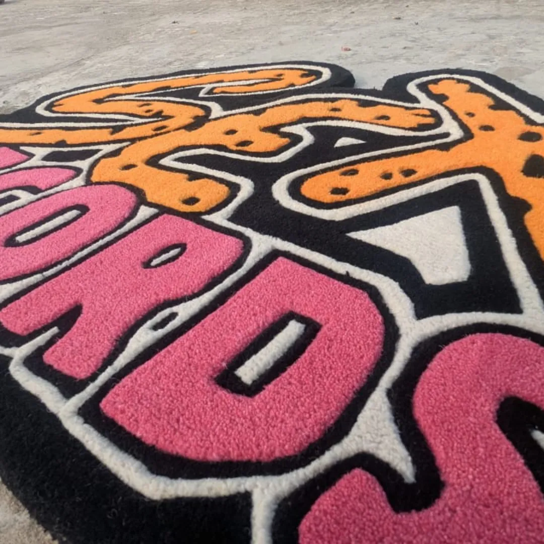 Close-up angled view of the Neon Graffiti rug, emphasizing the dense wool texture and the sharply carved, embossed details outlining the orange animal print and pink typography.