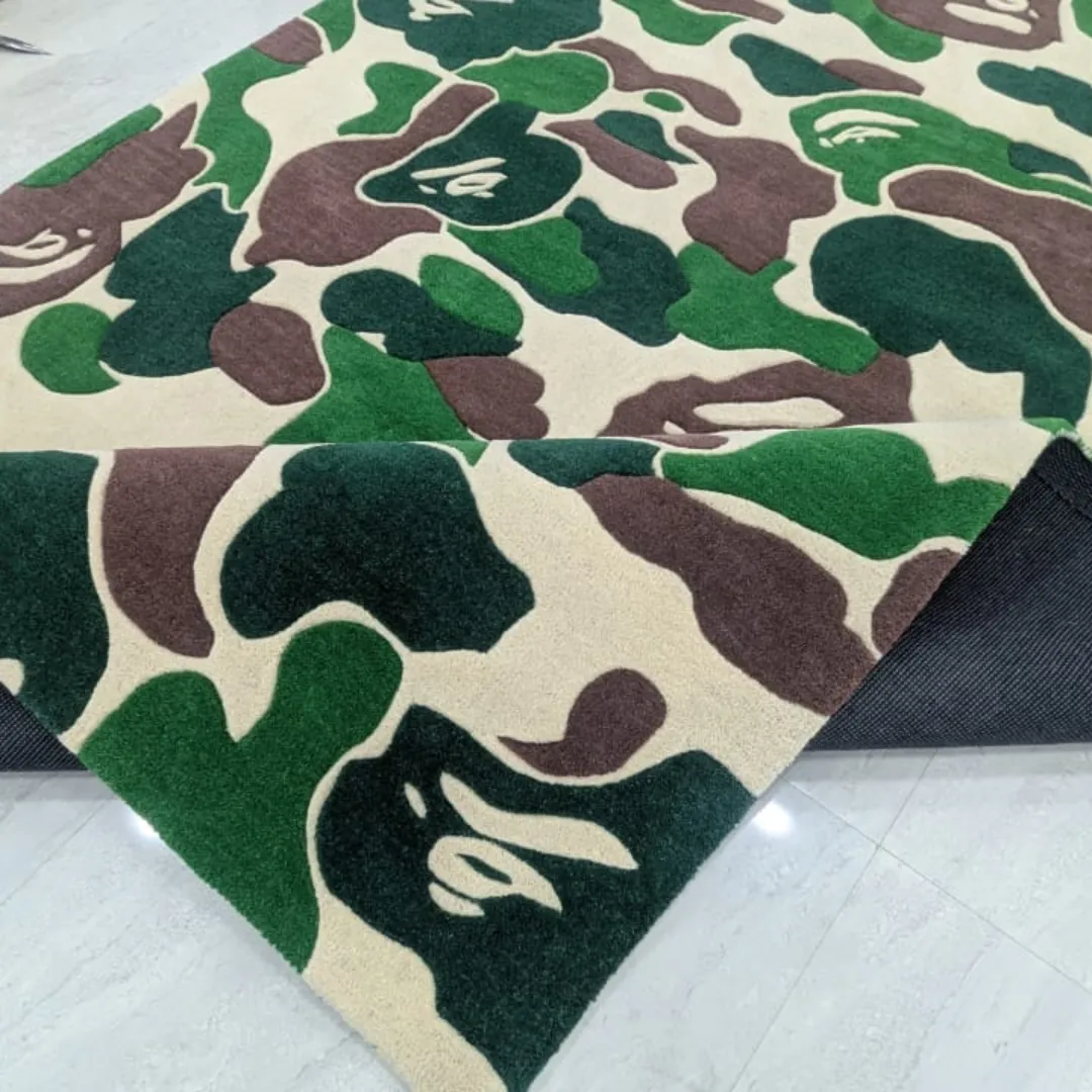 Angled view of the Shadowfield Camo Terrain rug with one corner folded back, revealing the black non-slip canvas backing underneath the thick green and brown patterned wool pile.