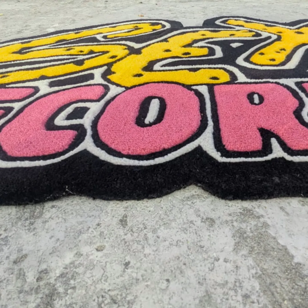 Extreme close-up low-angle view of the Vault Graffiti Drop rug on concrete, highlighting the thick, plush hand-tufted wool pile and the deep 3D carving that separates the bright pink lettering from the black base.