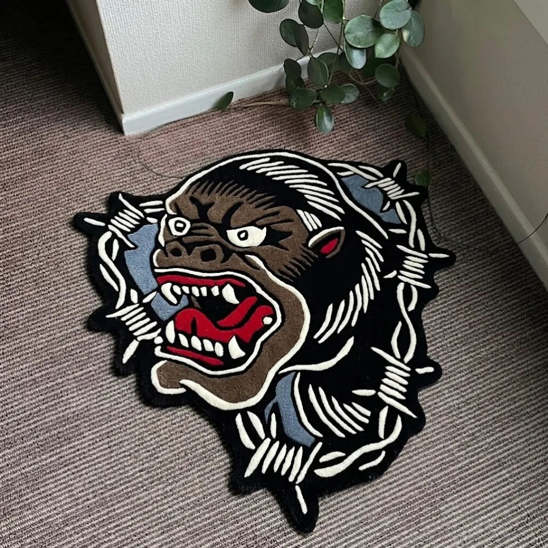 King Kong traditional tattoo style gorilla head shaped tufted area rug framed with barbed wire, displayed flat on a textured carpeted floor.