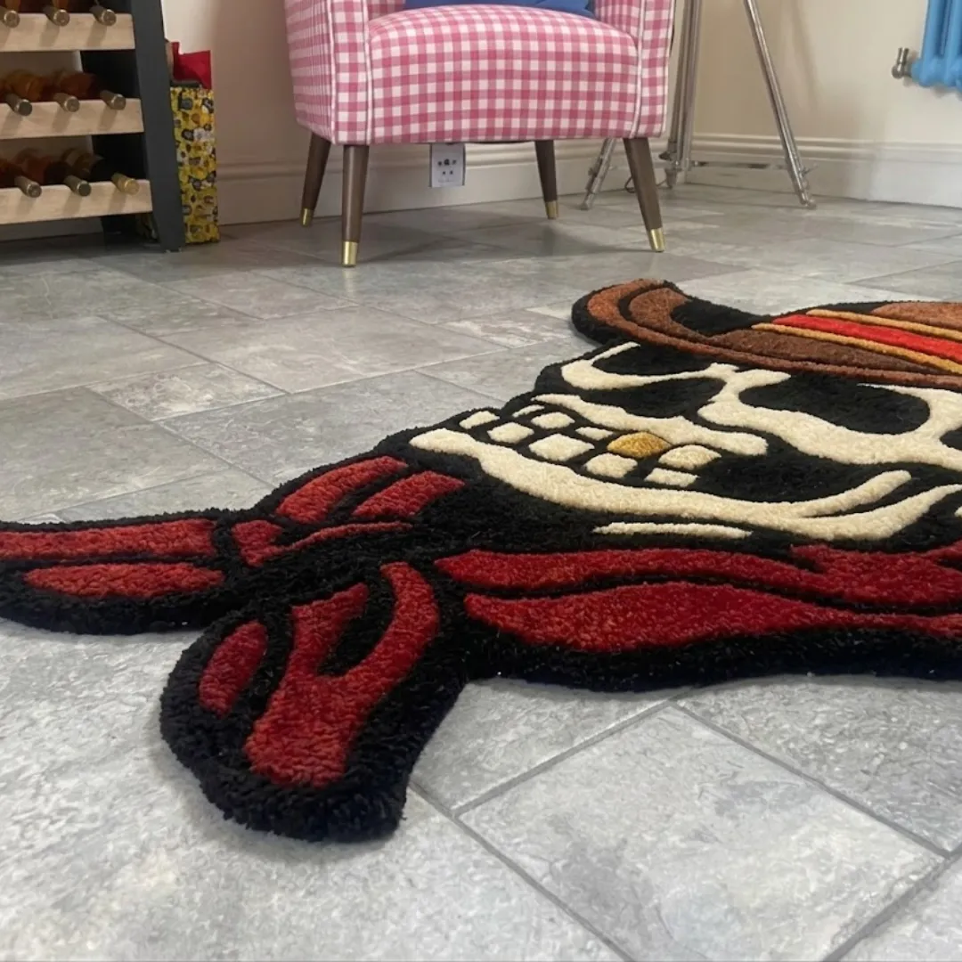 A low-angle, extreme close-up of the Skull Cowboy rug resting on a grey tiled floor. The detailed shot highlights the thick, plush tufted yarn texture of the red bandana and the skull's teeth, emphasizing the crisp lines of the American traditional tattoo aesthetic, with a pink checkered chair softly blurred in the background.
