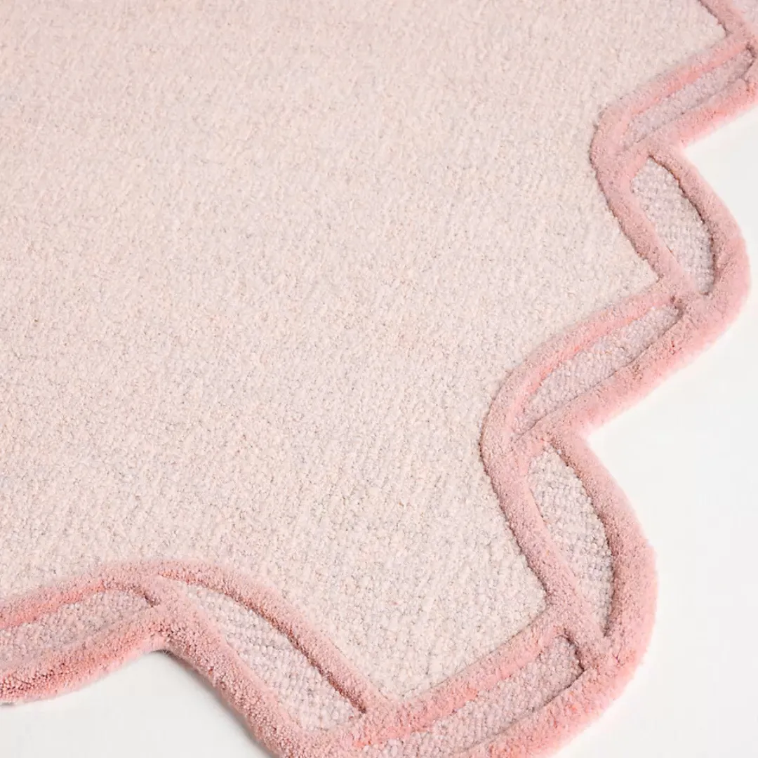 Close-up of pink rug showing curved scalloped edge and plush texture