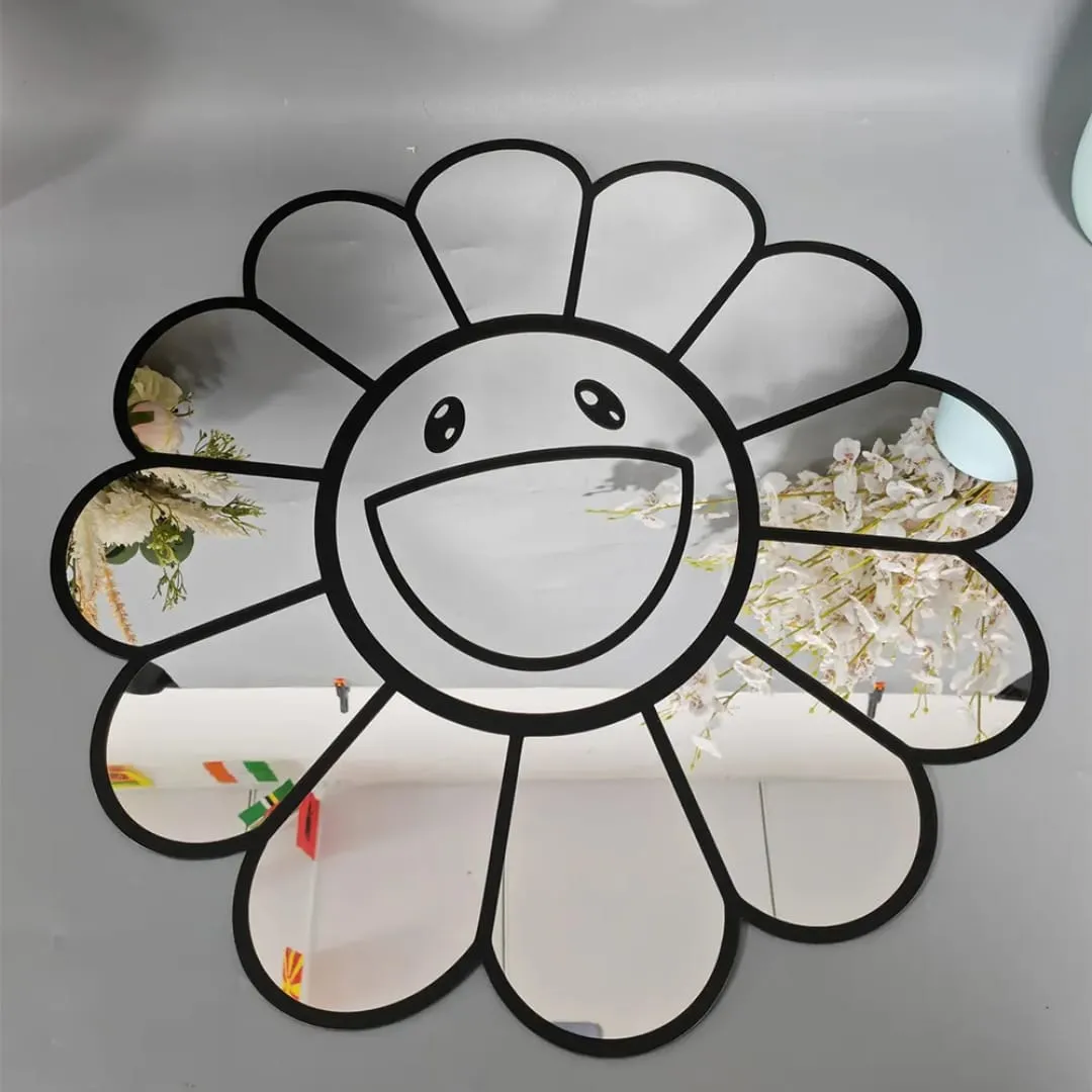 smiley daisy mirror floral reflection grey wall Straight-on view of the cute smiley daisy mirror resting against a light grey wall, reflecting white floral branches and bright room lighting across its glass petals.