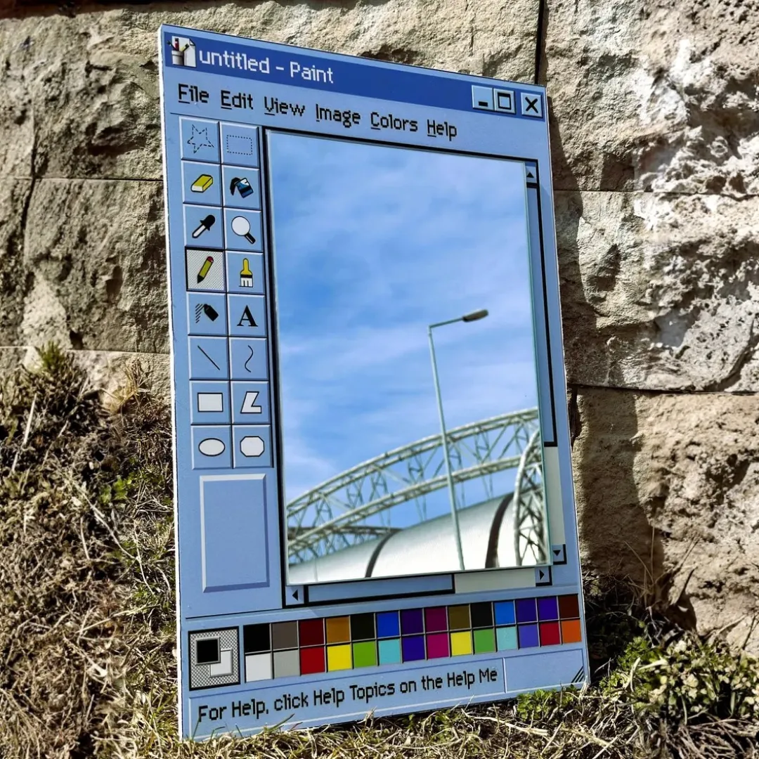 retro window paint app mirror outdoor setting A product shot of a retro-style window mirror designed as a vintage computer paint application, placed outdoors against a natural stone wall reflecting the sky.