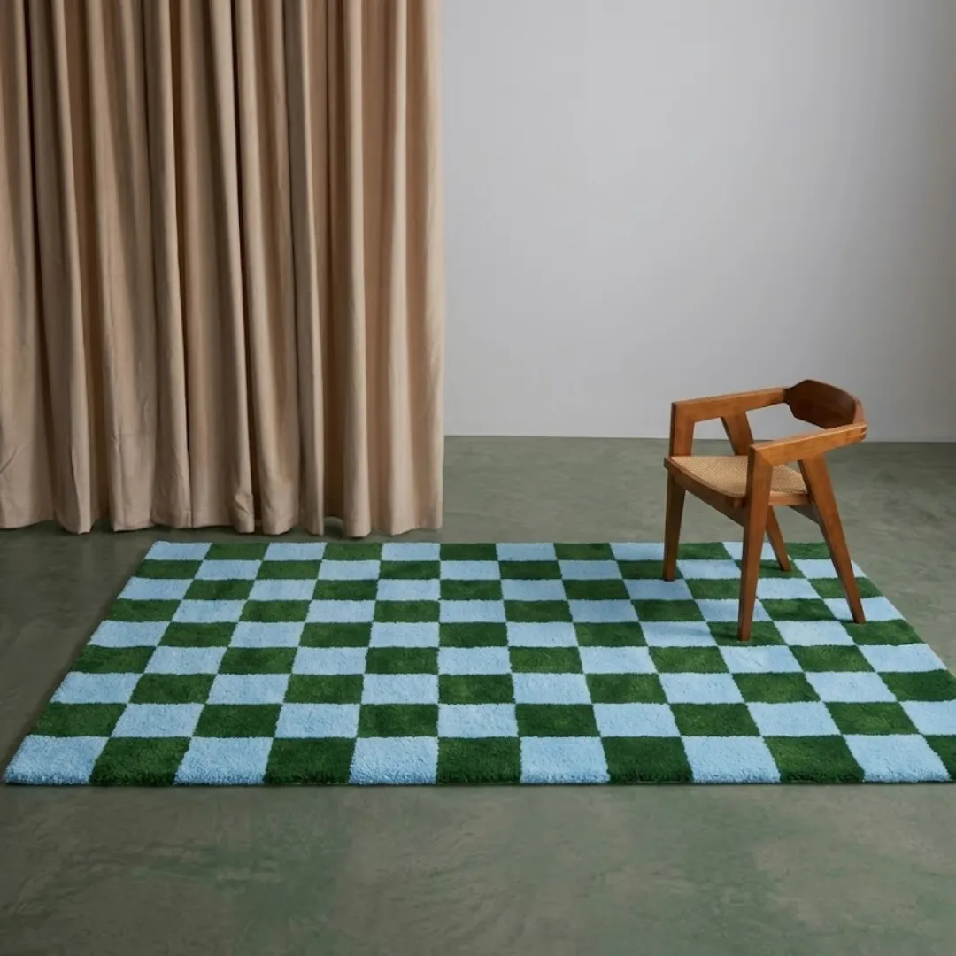 sage check geometric wool area rug interior styling An interior lifestyle shot of the rectangular Sage Check rug styled in a minimalist room with a wooden chair, light-colored curtains, and a clean, neutral floor.
