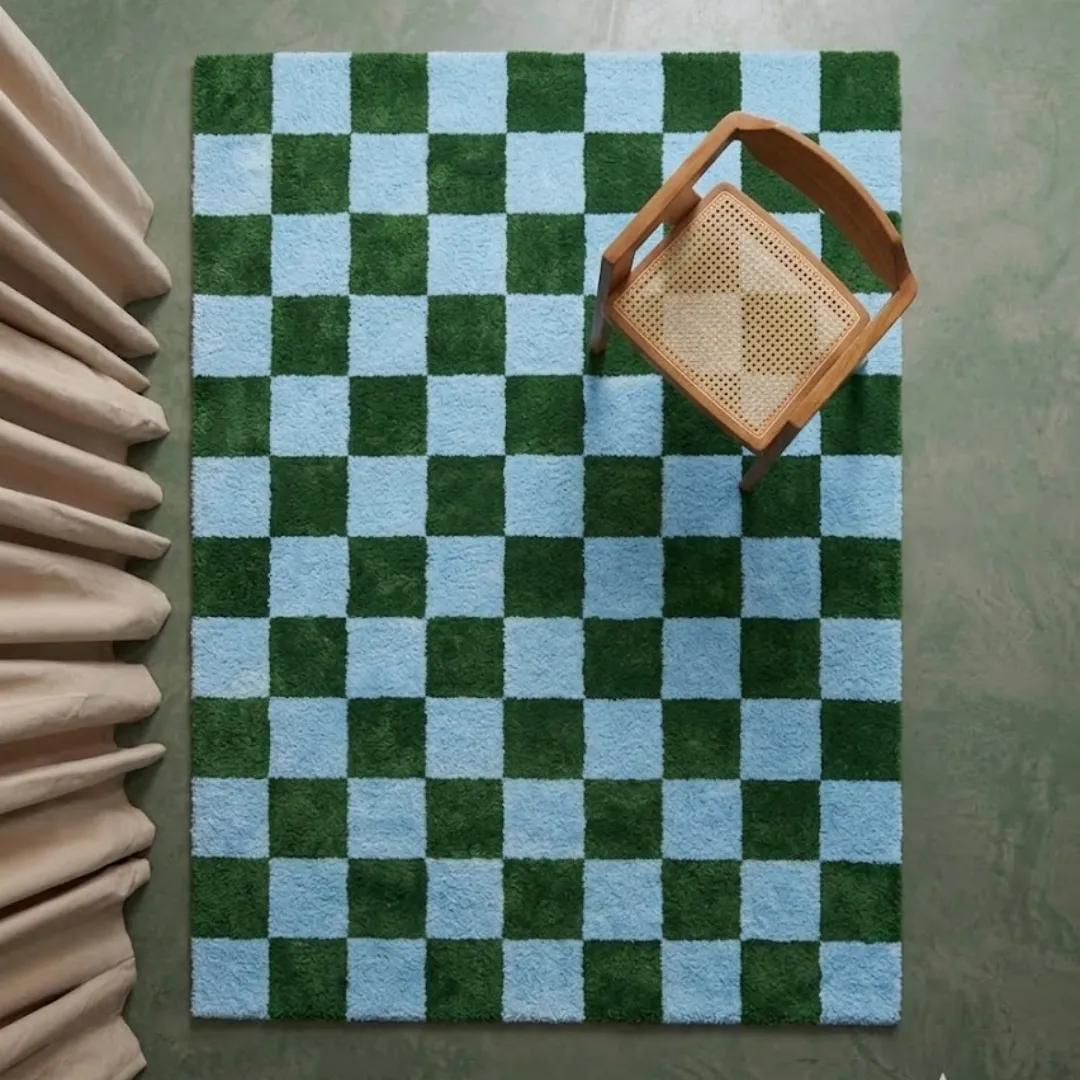 sage check geometric wool area rug top down interior A top-down perspective interior shot of the Sage Check rug positioned on a smooth floor near a wooden chair and soft drapery, highlighting the vivid checkerboard design.