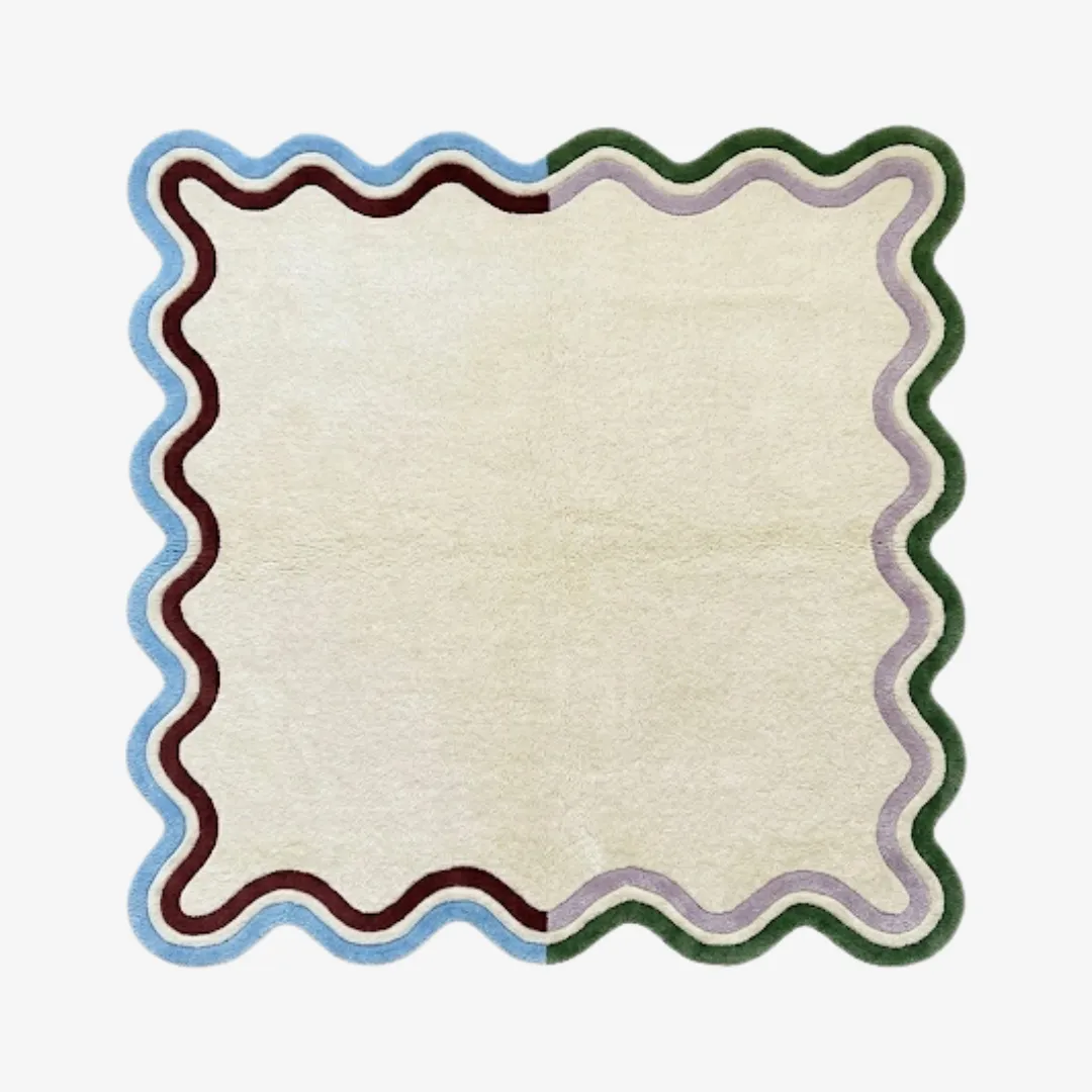 serena scalloped edge rug product shot A top-down studio product photograph of the rectangular Serena rug, featuring a cream-colored center and a distinctive wavy scalloped border in blue, maroon, purple, and green.