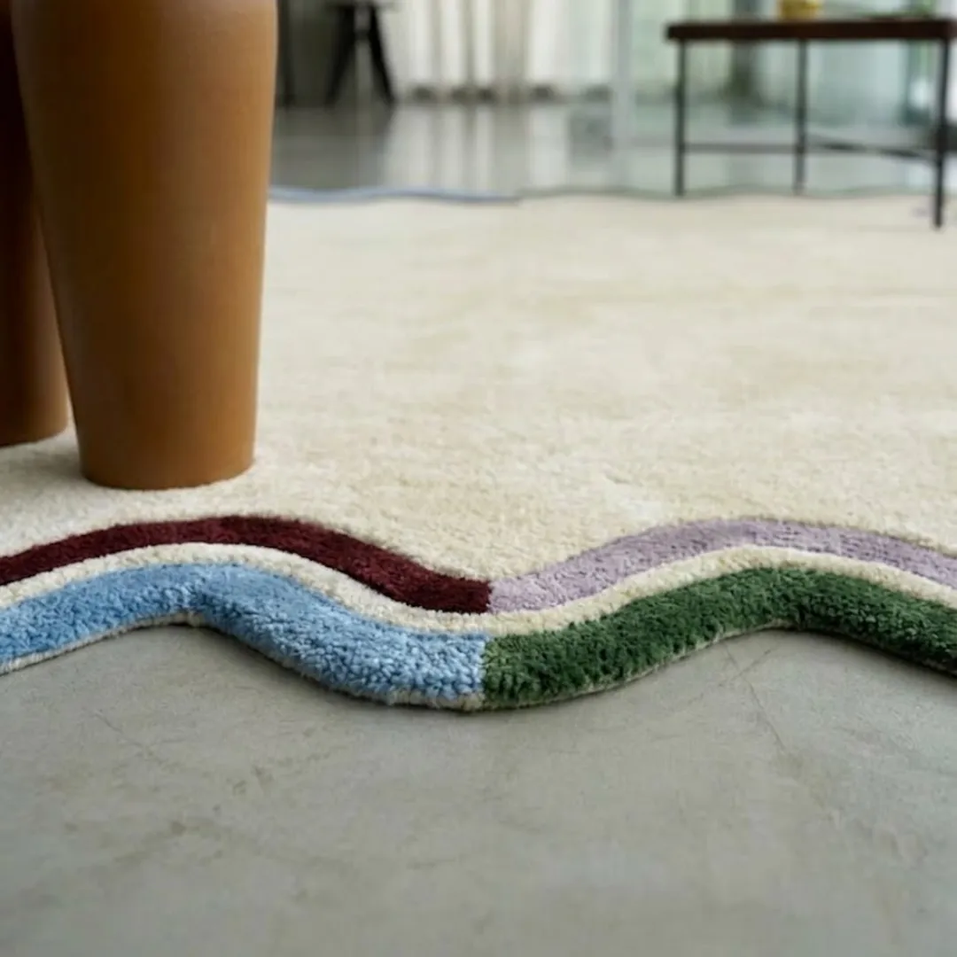 serena scalloped edge rug texture close up A close-up view of the Serena rug, focusing on the textured, wavy scalloped edges in layers of blue, maroon, purple, and green against a cream-colored wool pile.