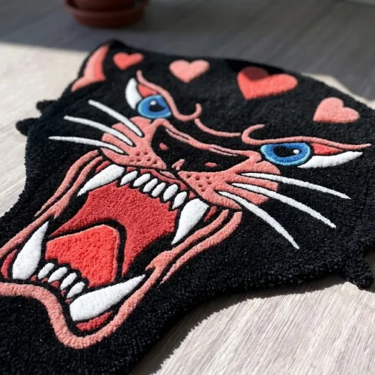pink panther head rug texture close up Close up angled view of a black panther head rug highlighting the textured yarn details of the pink roaring mouth and white teeth.
