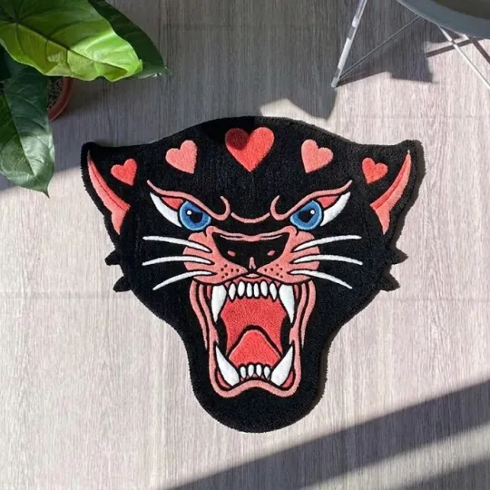 pink panther head rug top down Overhead view of a black panther head shaped rug featuring traditional tattoo style pink accents next to a green potted plant.