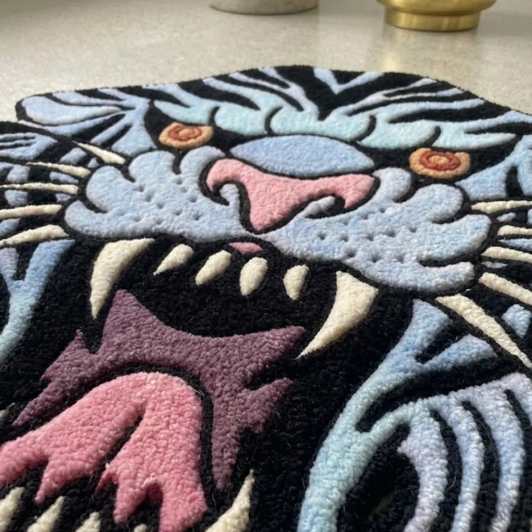 rebellion blue rug close up texture An extreme close-up of the Rebellion Blue Rug, focusing on the tiger's open mouth, sharp white teeth, and pink tongue. The detailed shot emphasizes the high-quality tufted yarn of the light blue fur and black stripes in the classic tattoo art style.