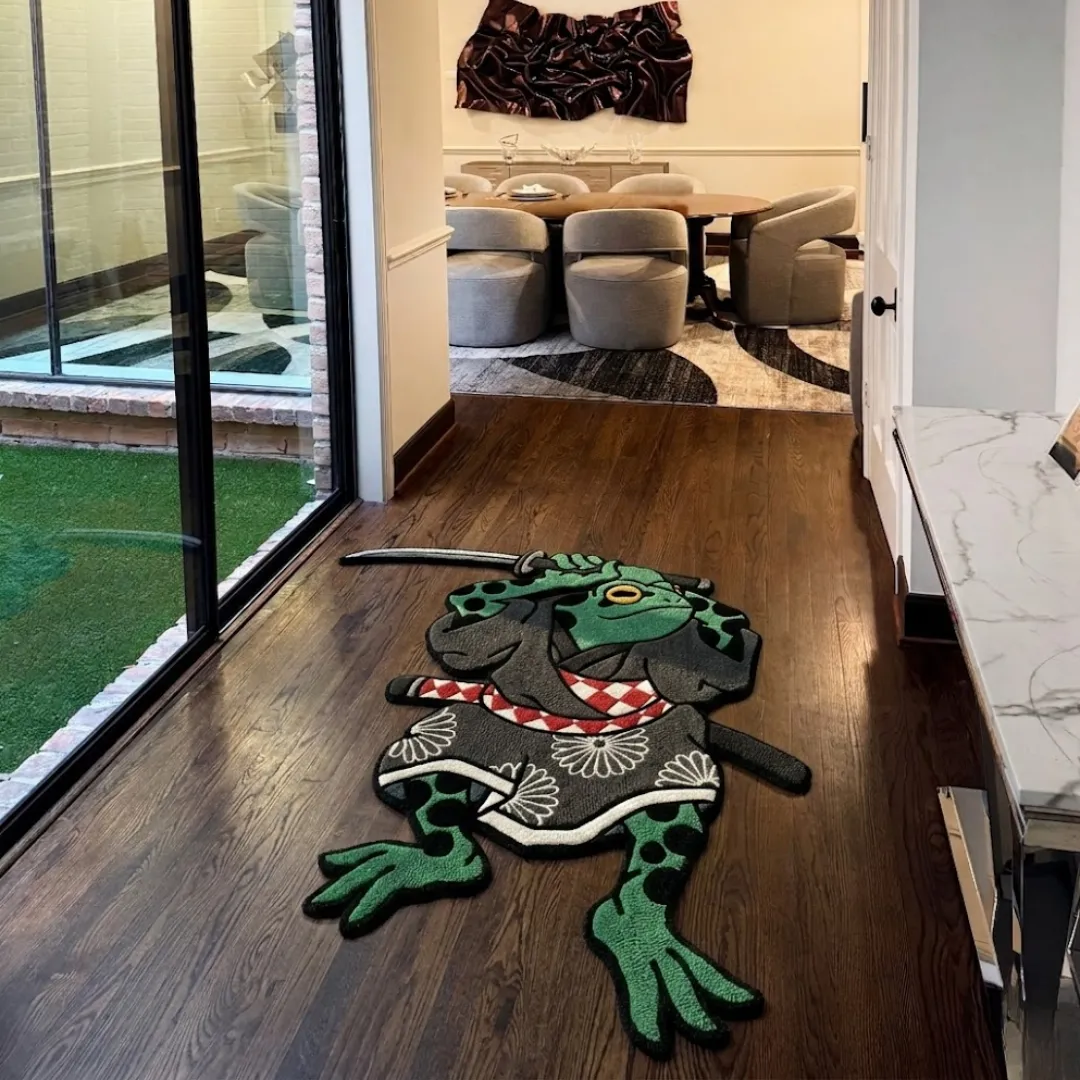 kaeru no bujin japanese rug hallway setting An angled view of the Kaeru No Bujin Japanese Rug placed on a dark hardwood floor in a modern hallway. The hand-tufted custom rug features a traditional Japanese tattoo design of a green samurai frog holding a katana, wearing a dark grey kimono with white floral patterns and a red and white checkered sash, positioned near sliding glass doors looking toward a contemporary dining room.