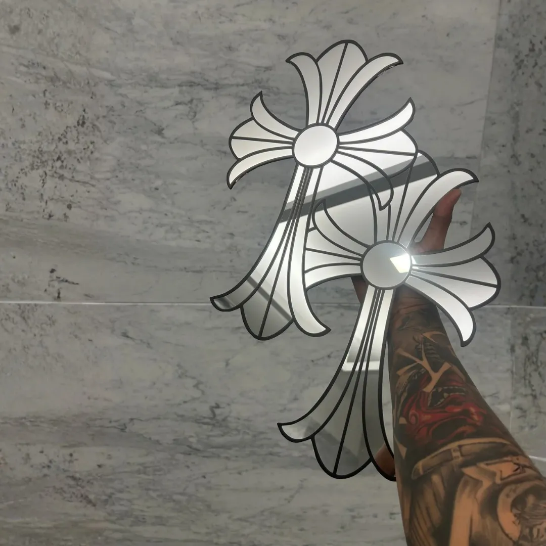 gothic cross mirrors hand held marble A tattooed hand holding up two gothic cross-shaped mirrors against a white marble wall, capturing bright light reflections on the glass surfaces.