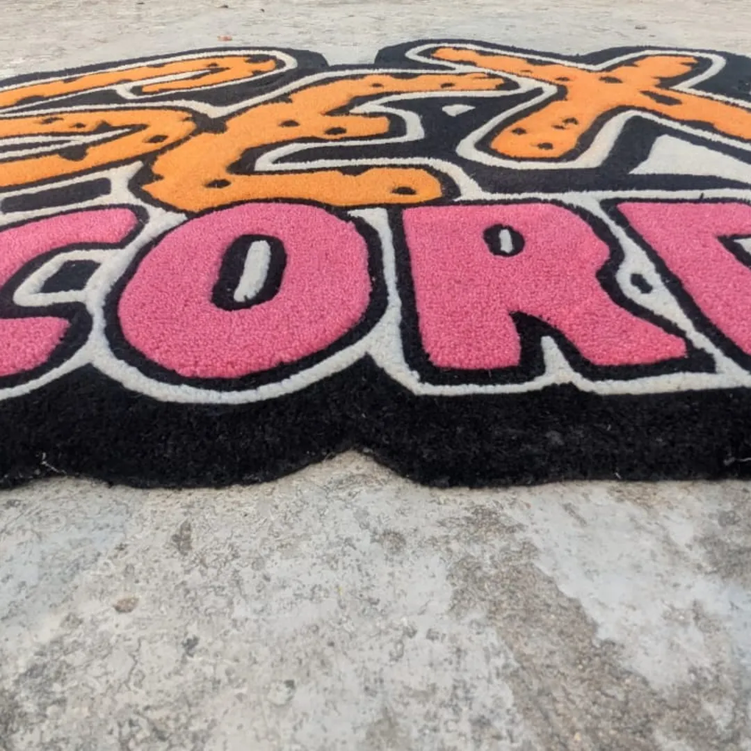 neon graffiti rug edge Extreme close-up low-angle view of the Neon Graffiti rug on concrete, highlighting the thick, plush hand-tufted wool pile and the deep 3D carving that separates the bright pink lettering from the black base.