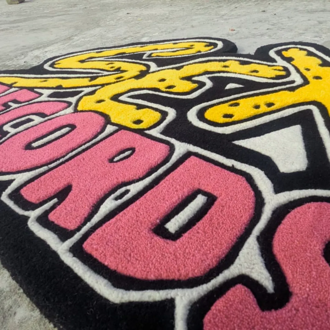 vault graffiti drop rug texture Close-up angled view of the Vault Graffiti Drop rug, emphasizing the dense wool texture and the sharply carved, embossed details outlining the yellow animal print and pink typography.
