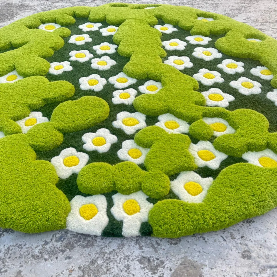 3d moss rug angled view Angled shot of the round 3-D Moss Rug displayed on a concrete floor. The lower perspective emphasizes the three-dimensional, multi-level tufting, showing how the bright green cloud-like moss shapes pop out from the floral daisy background.
