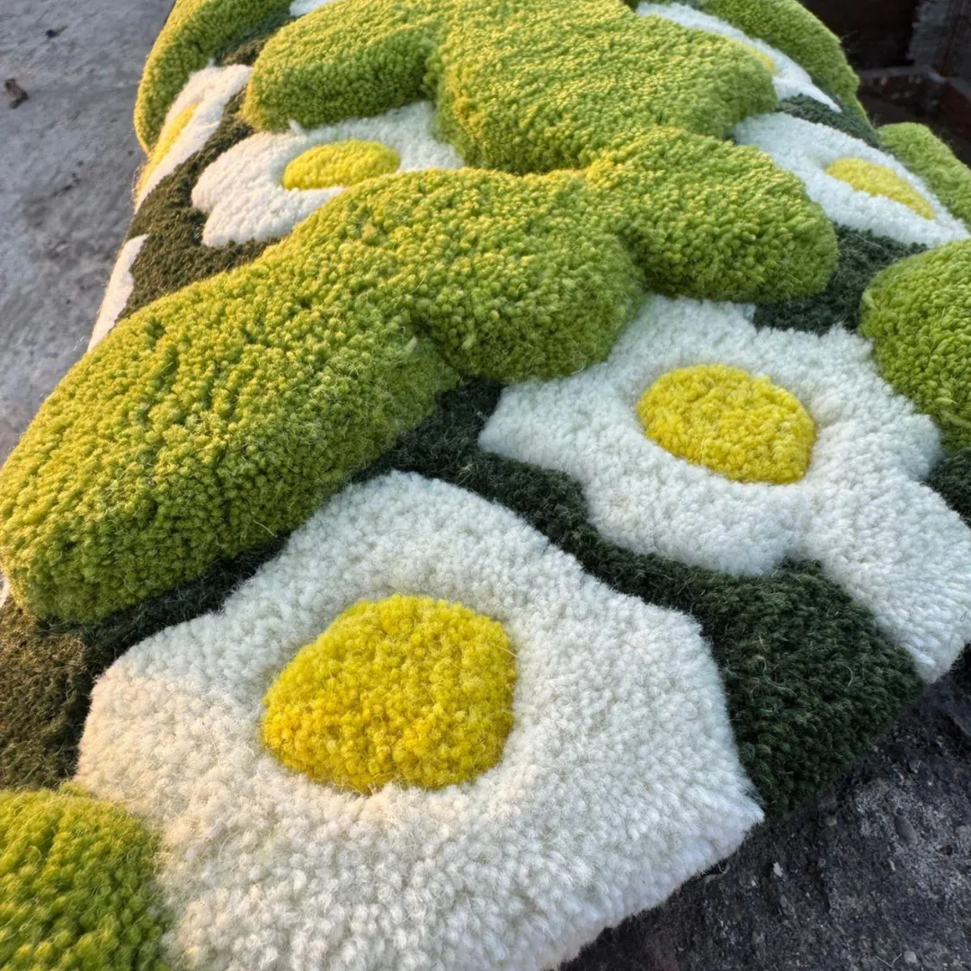 3d moss rug close up texture An extreme close-up of the 3-D Moss Rug taken in warm sunlight, highlighting the different pile heights of the tufted yarn. The image focuses on the highly textured, raised bright green moss patches and the plush white daisies with yellow centers.