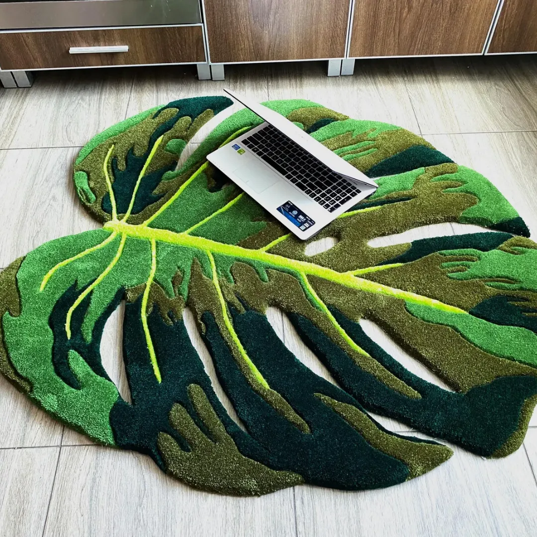 monstera flux rug angled view with laptop Angled shot of the Monstera Flux Rug, a custom split-leaf tropical design in vibrant greens, placed on a tiled kitchen floor with an open laptop sitting on top.