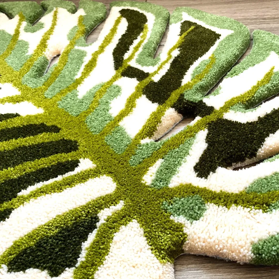 verdant monstera rug center detail Close-up view of the Verdant Monstera Rug's scalloped outer edges, showing the intricate cut-out leaf details and the dense, high-quality tufted yarn in cream, dark green, and light green shades.
