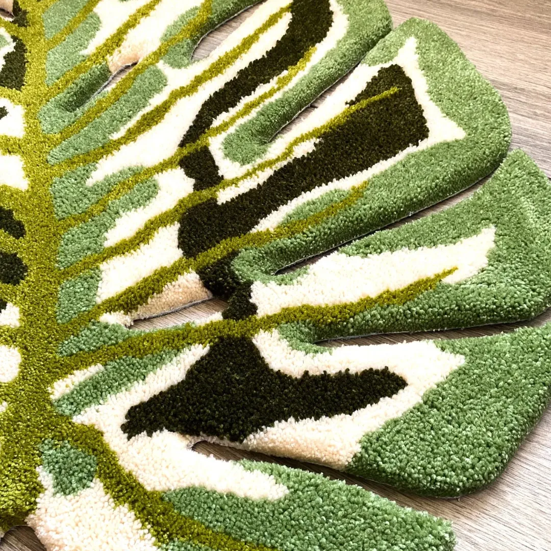 verdant monstera rug edge close up A detailed close-up of the Verdant Monstera Rug, highlighting the thick tufted texture of the central bright green vein intersecting with plush cream, light green, and dark green leaf patterns.