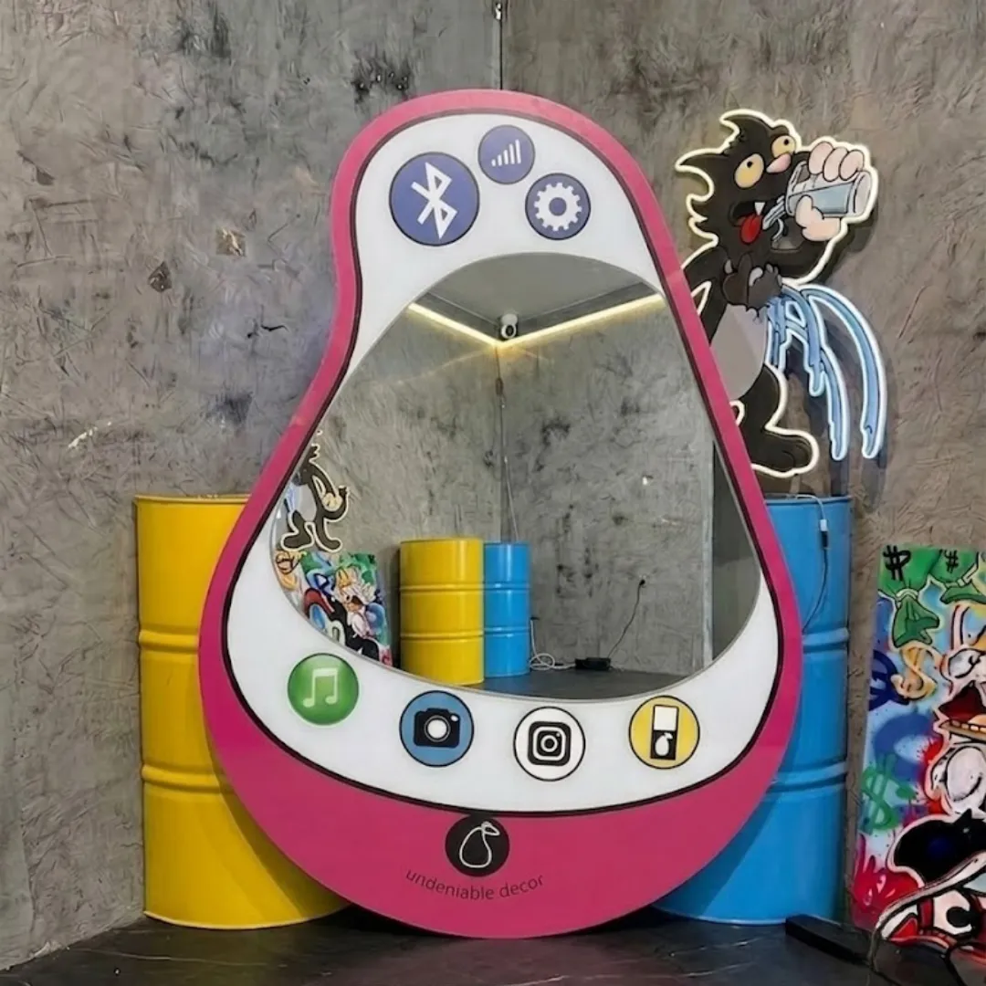aura pear phone mirror pop art room styling Interior styling view of the Aura Pear Phone Mirror displayed in a creative pop art studio space flanked by bright yellow and blue industrial barrels and glowing neon cartoon wall decor.