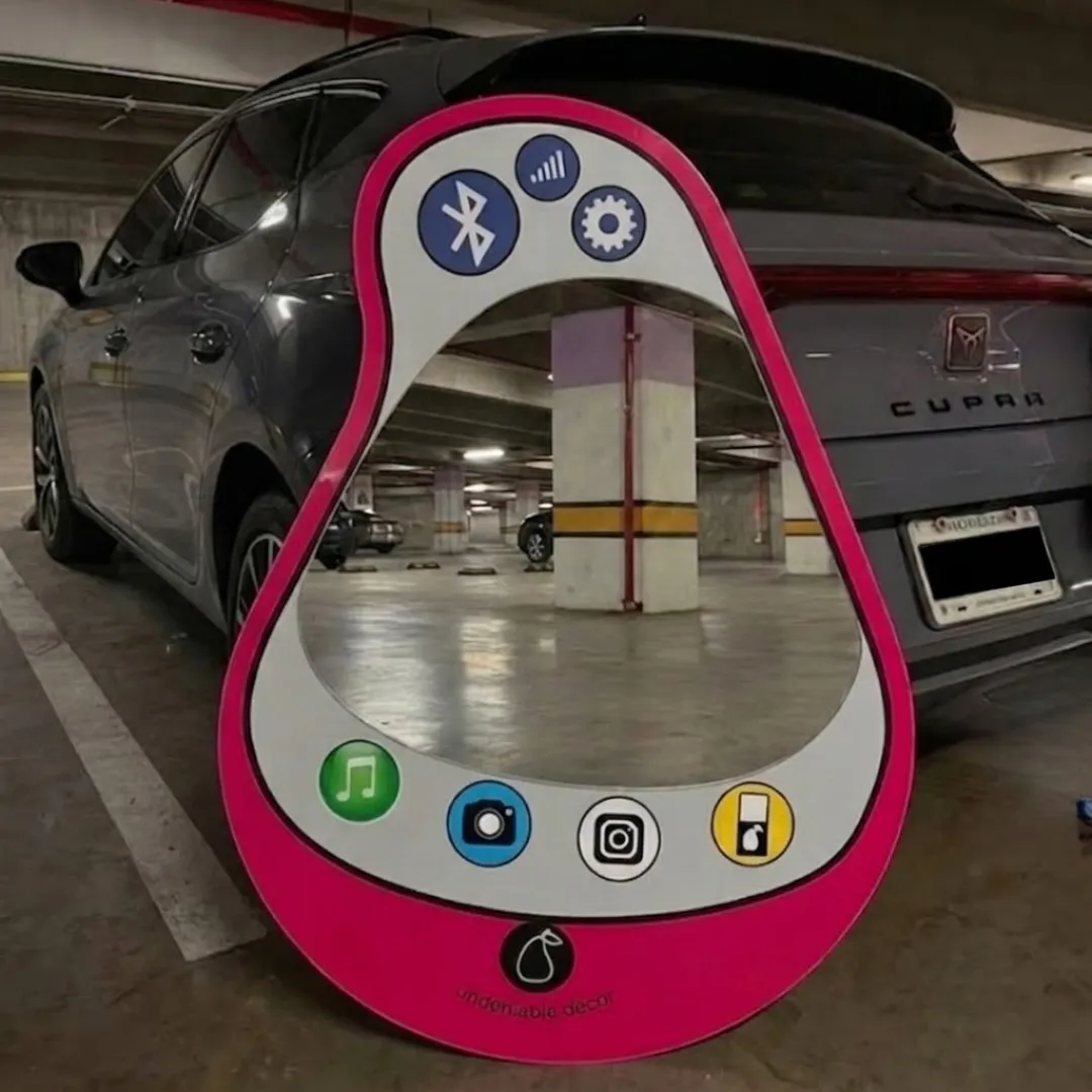 aura pear phone mirror urban garage lifestyle Wide angle lifestyle shot of the hot pink Aura Pear Phone Mirror resting on the floor of a concrete underground parking garage, reflecting the interior columns and a grey vehicle.