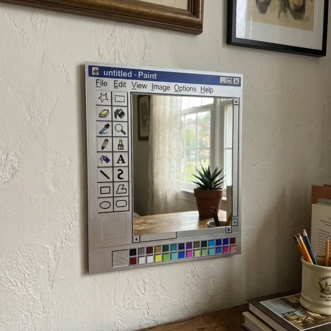 paint window retro computer art mirror desk arrangement An interior lifestyle view of a Paint Window mirror mounted on a white wall above a wooden desk, reflecting a window with a potted succulent, surrounded by a pencil holder and stacked books.