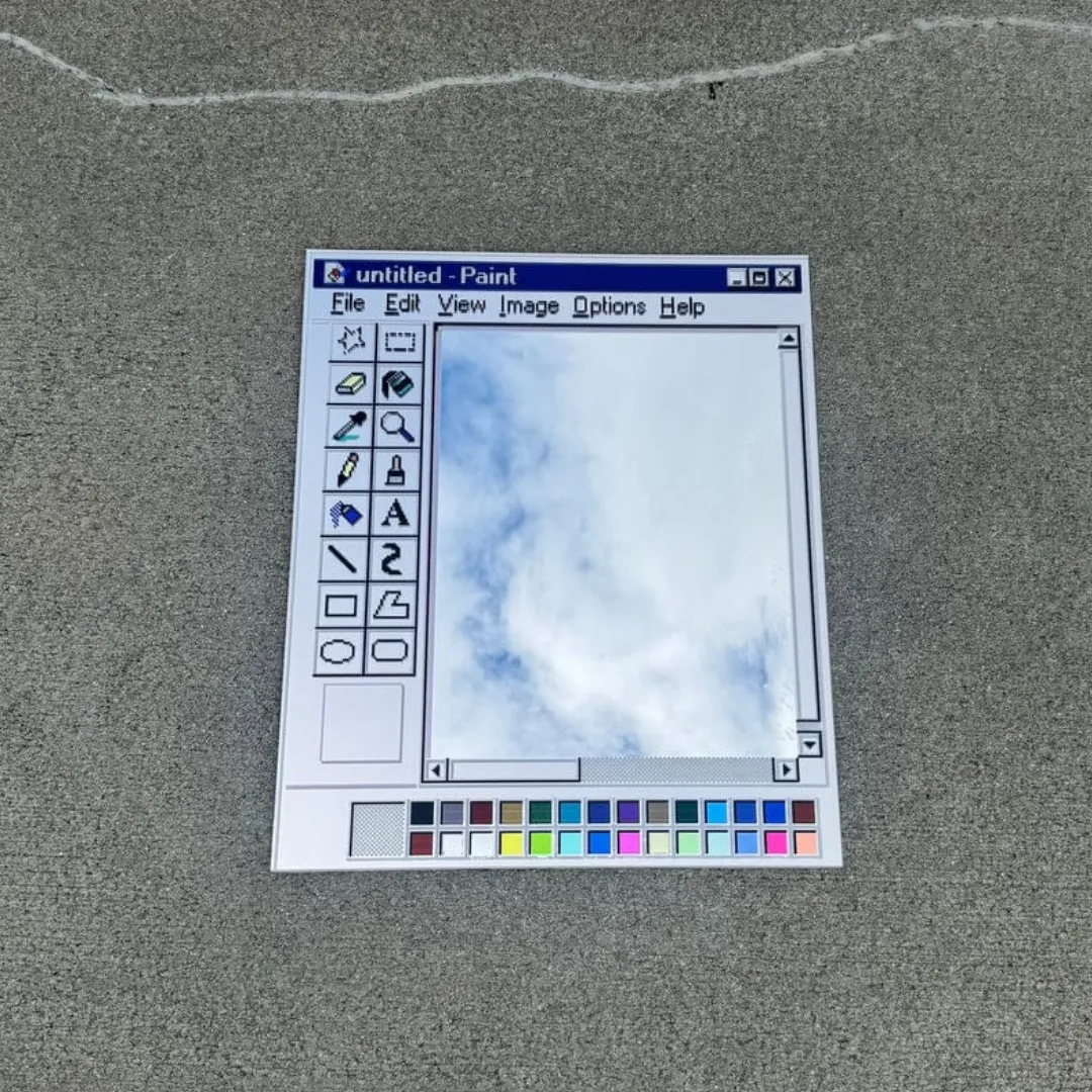 paint window retro computer art mirror product shot A high-angle close-up product shot of a Paint Window mirror isolated on a grey concrete surface, featuring a classic vintage computer paint software interface frame and a clear reflective glass mirror center.