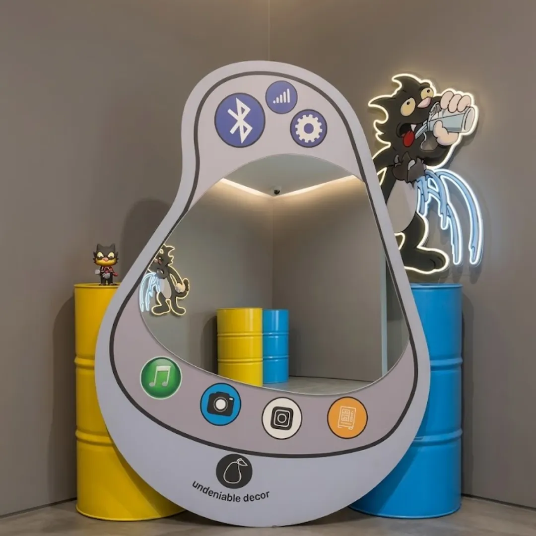 pear frame phone mirror whimsical pop art decor Floor-standing Pear Frame mirror featuring a whimsical pear-shaped border, retro smartphone app icons, and a glossy mirror surface, styled in a playful studio space between vibrant yellow and blue industrial barrels with neon cat-themed wall art.