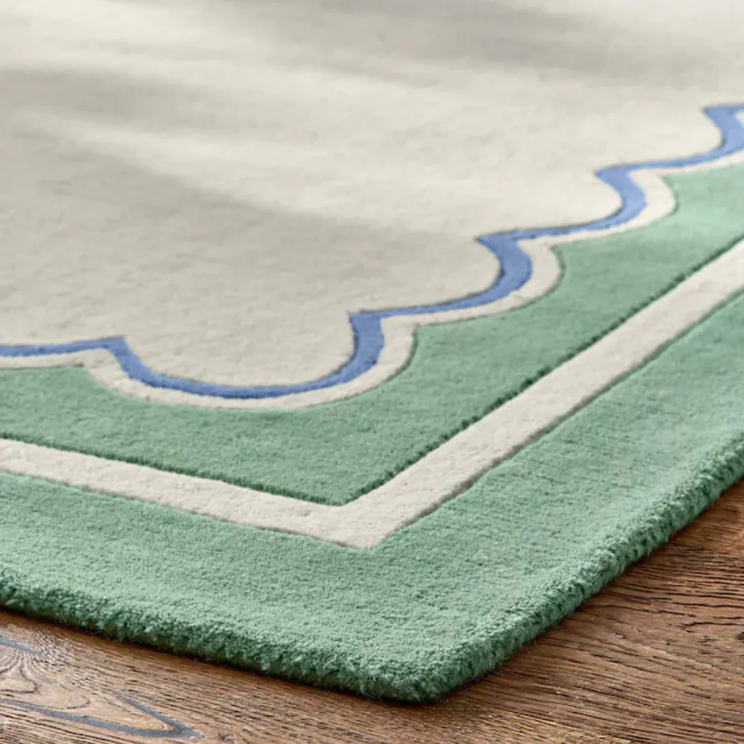 Close-up of green and blue scalloped edge on cream rug surface