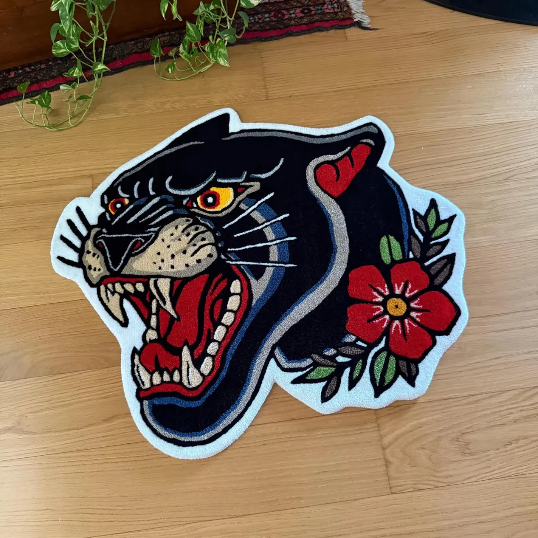 Hand tufted rug of a snarling black panther head with floral tattoo design in red, green, and white on a wooden floor.