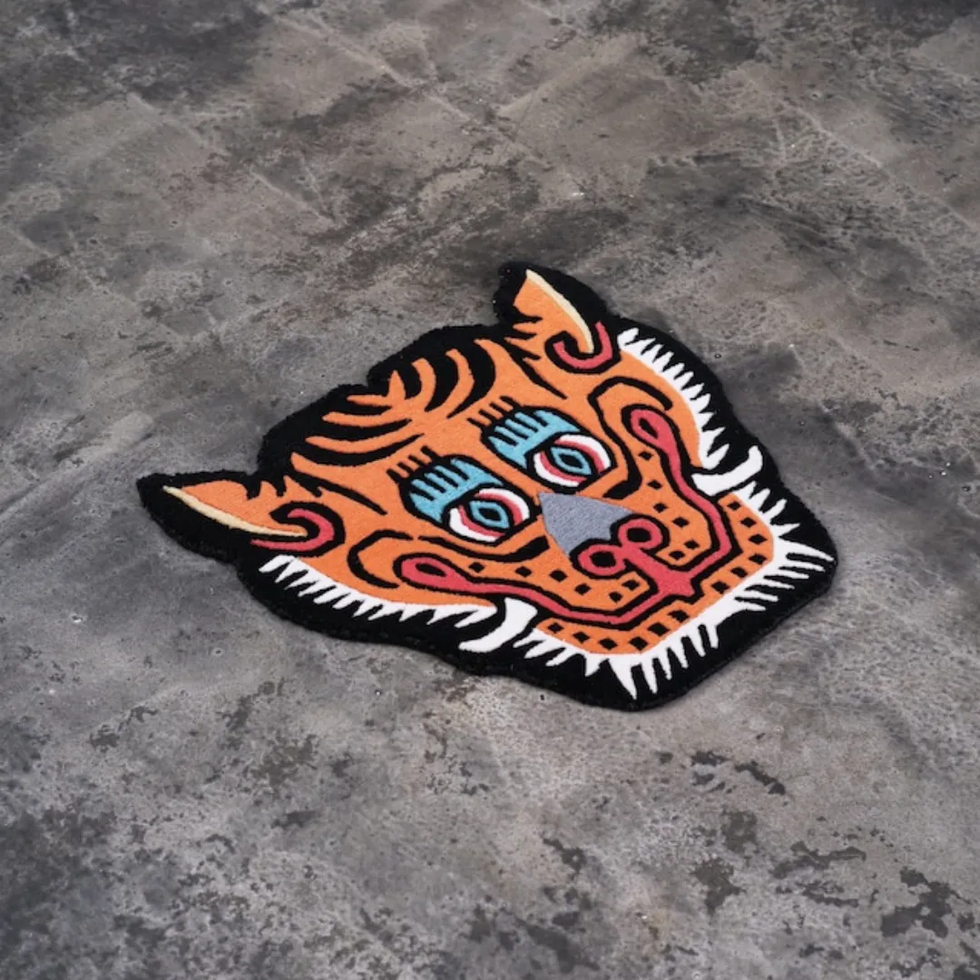 and tufted tiger face rug in orange, red, and black with bold eyes and stylized Tibetan design.