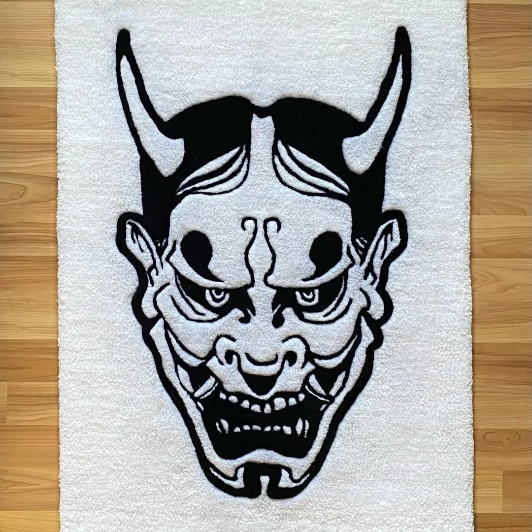 Rectangular white rug showcasing a striking black Hannya mask with curved horns and a menacing expression, laid flat on wooden flooring.