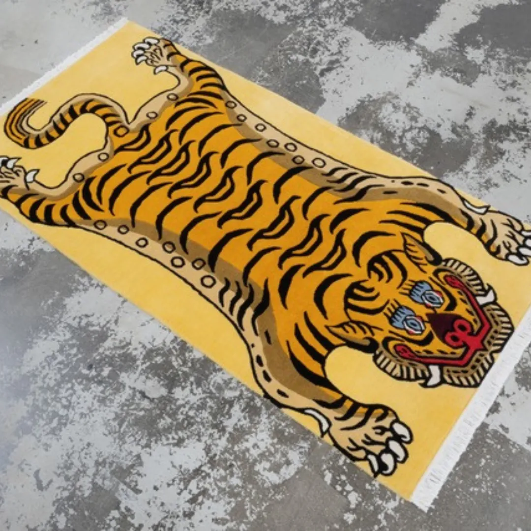 Yellow Tibetan-style tiger rug with bold black stripes, red face details, and white fringe, displayed on a gray concrete floor.