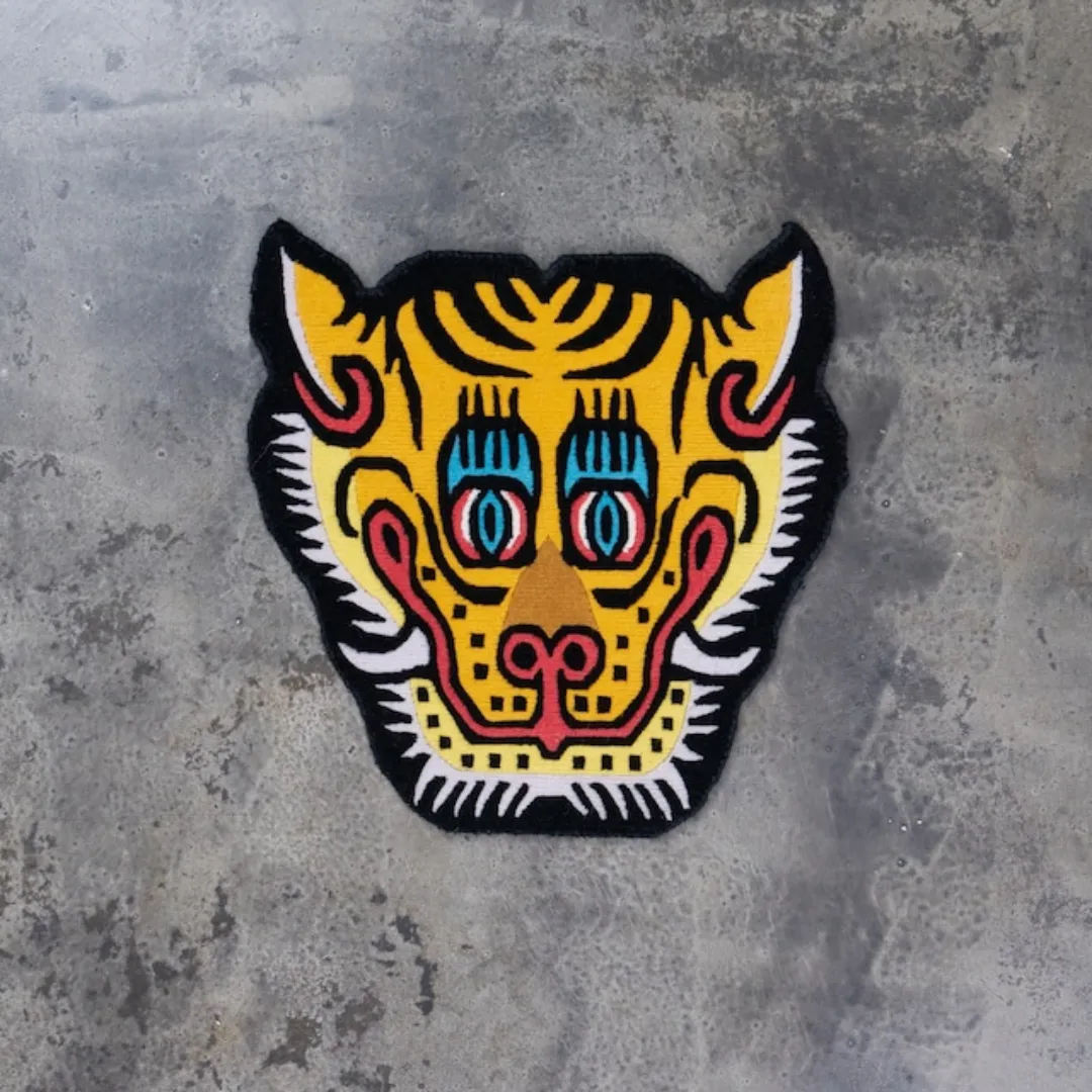 Hand tufted tiger face rug in yellow, red, and black with bold eyes and stylized Tibetan design.