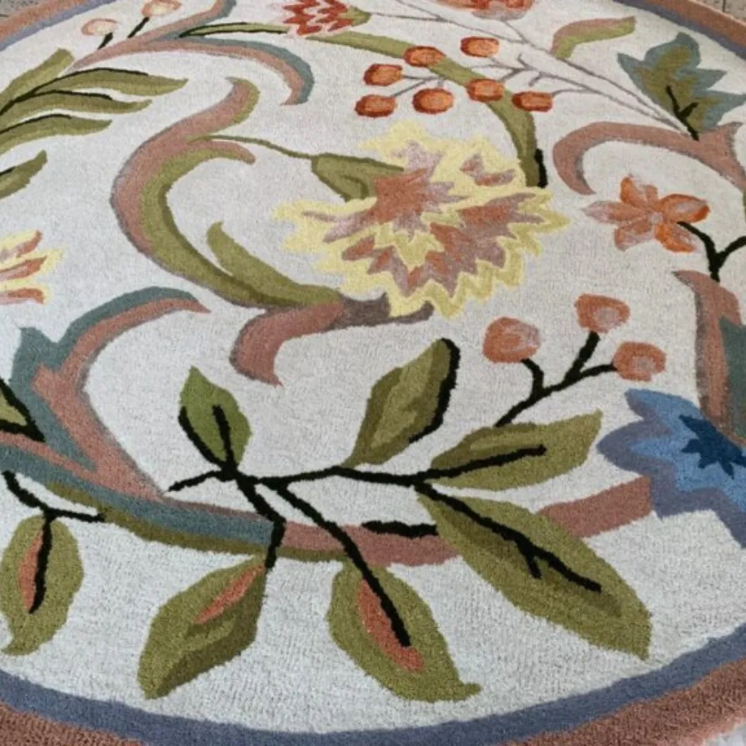 Hand-tufted round rug with a botanical design in orange, green, and blue.