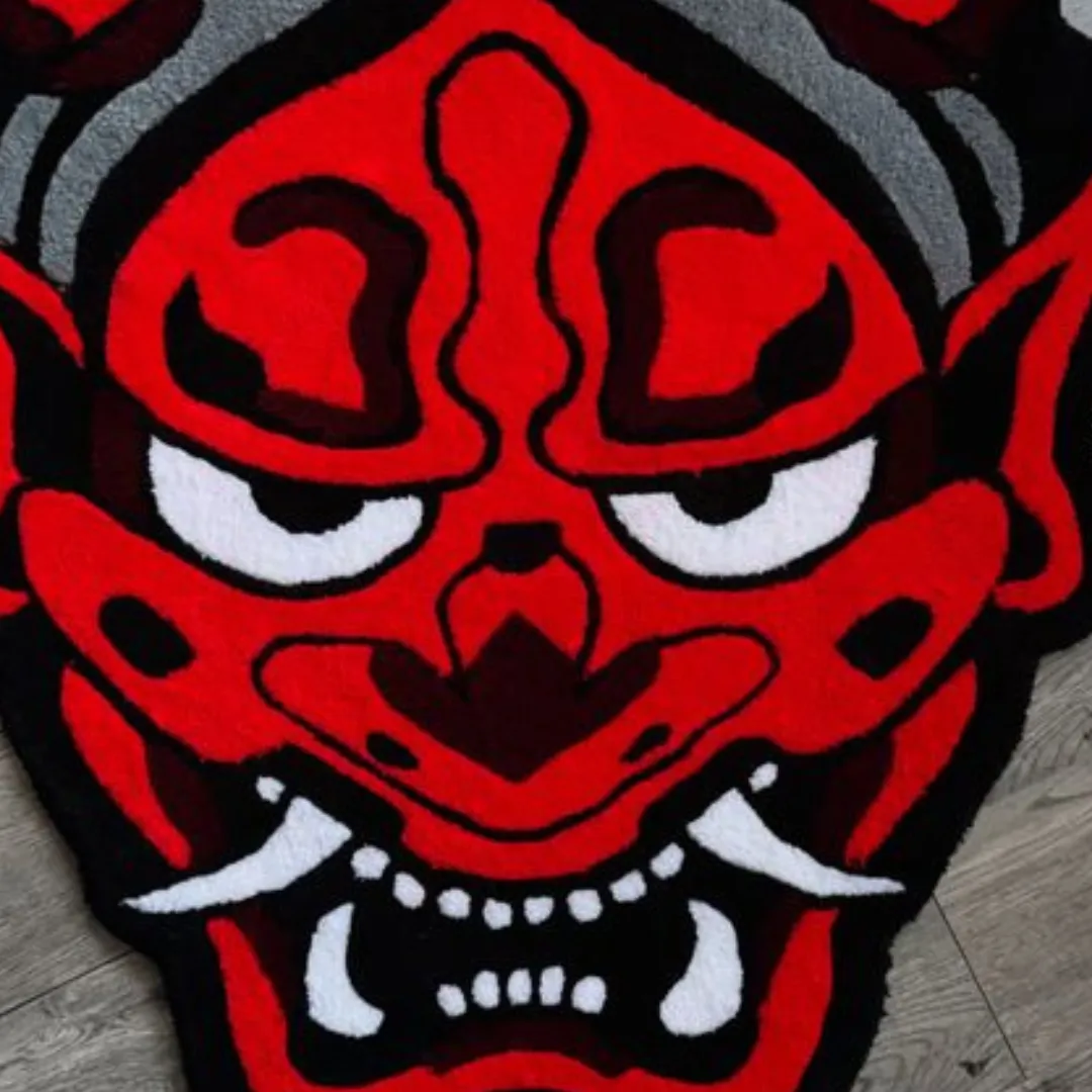 Red hand tufted Oni mask rug with bold black outlines, horns, and tusks on a wooden floor background.